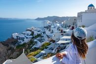 A young girl gazes over the stunning white buildings and blue sea of Santorini, Greece, capturing travel and serene beauty.
