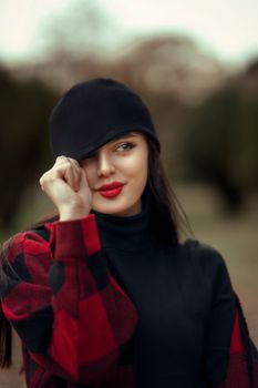 A sophisticated woman in a black turtleneck and checkered jacket poses outdoors, exuding elegance and charm.