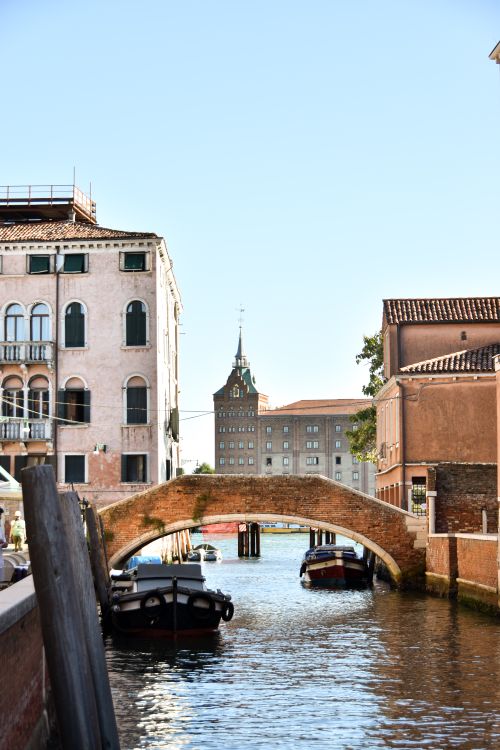 Free Idyllic view of a Venetian canal with a classic stone bridge under a clear sky. Stock Photo