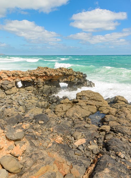 Free A scenic view of rocky seashore with waves crashing under a bright blue sky. Stock Photo