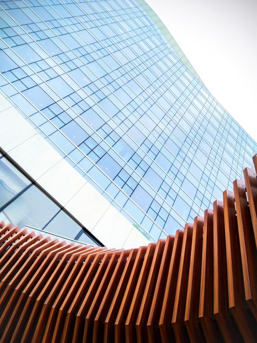 Free Low-angle view of a contemporary skyscraper facade with wooden architectural elements in the foreground. Stock Photo