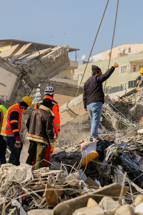 Emergency responders in hard hats examining collapsed concrete rubble after an earthquake