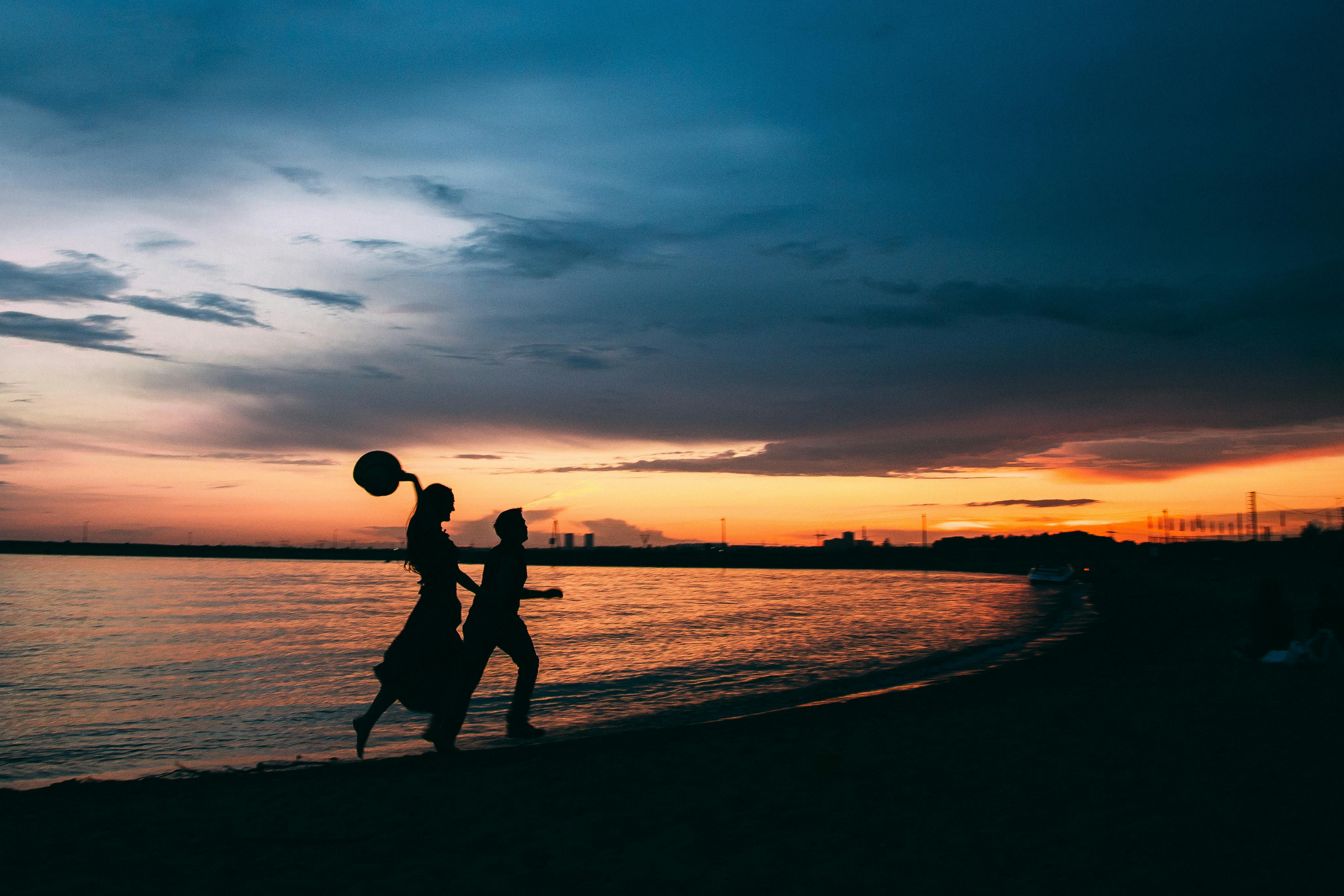 two people running on the beach at sunset