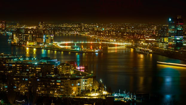 Vibrant cityscape at night with illuminated buildings and reflections on the water.
