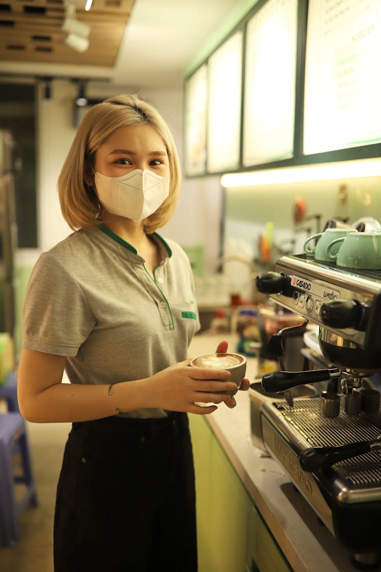 Bartender With A Medical Mask Standing With Cup Of A Cappuccino At The Coffeemaker