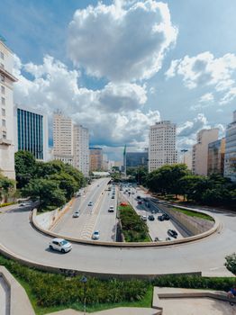 A vibrant urban landscape featuring skyscrapers, road traffic, and greenery under a cloudy sky.