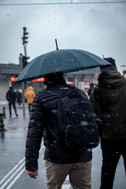 Free Man walking with an umbrella during snowfall in a city, capturing a winter urban scene. Stock Photo