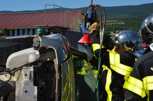Firefighters in helmets and uniforms conducting an extrication on an overturned vehicle outdoors.