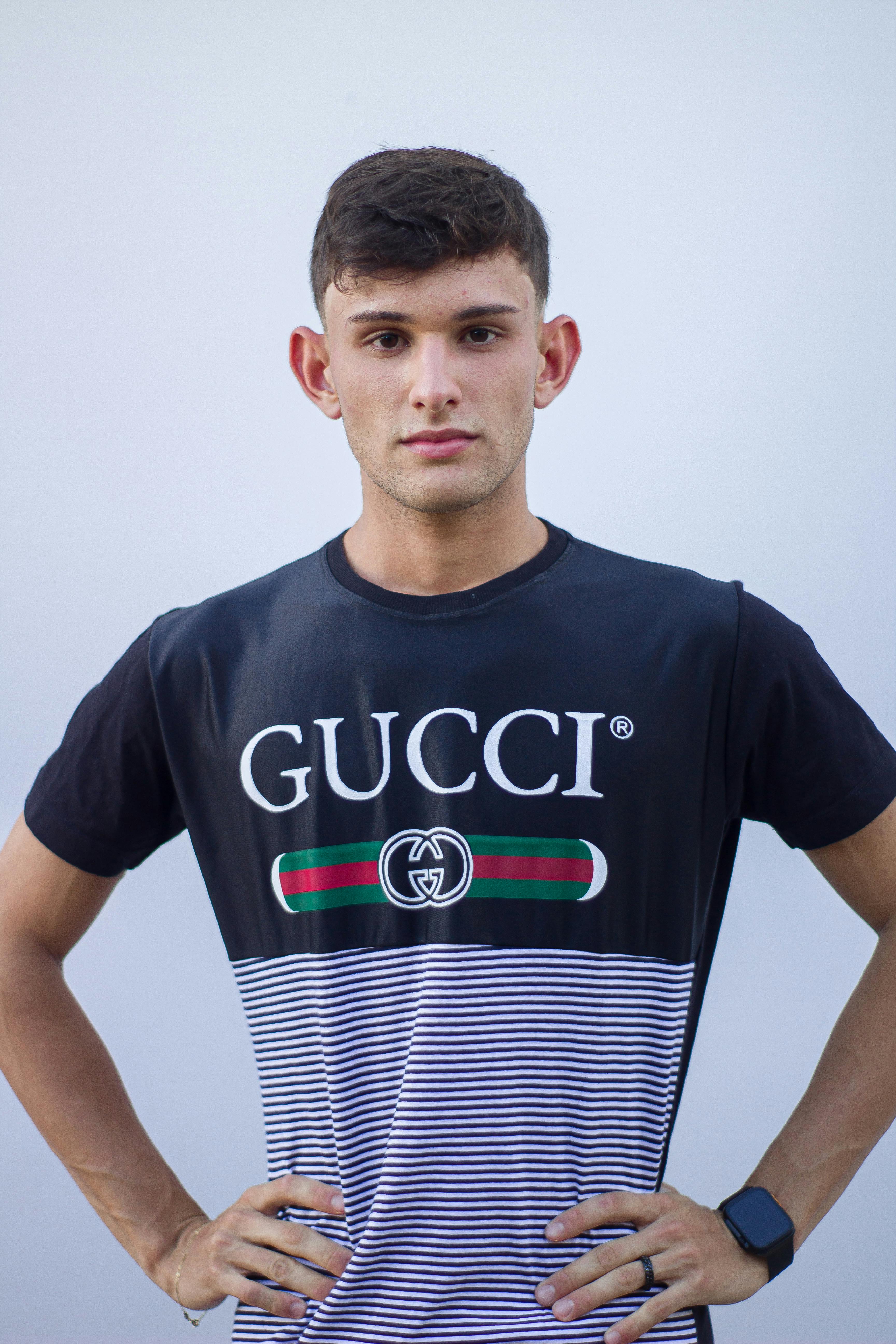 Young adult male wearing a Gucci t-shirt, posing confidently in a studio setting.