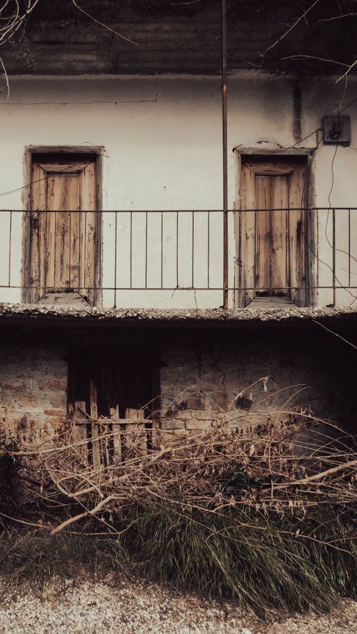 Free A rustic abandoned house showing weathered doors and an overgrown balcony. Perfect for texture and decay concepts. Stock Photo