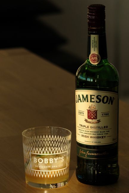 A glass tumbler of amber Irish whiskey beside an open bottle and a small dish of brown sugar on a dark wood bar counter