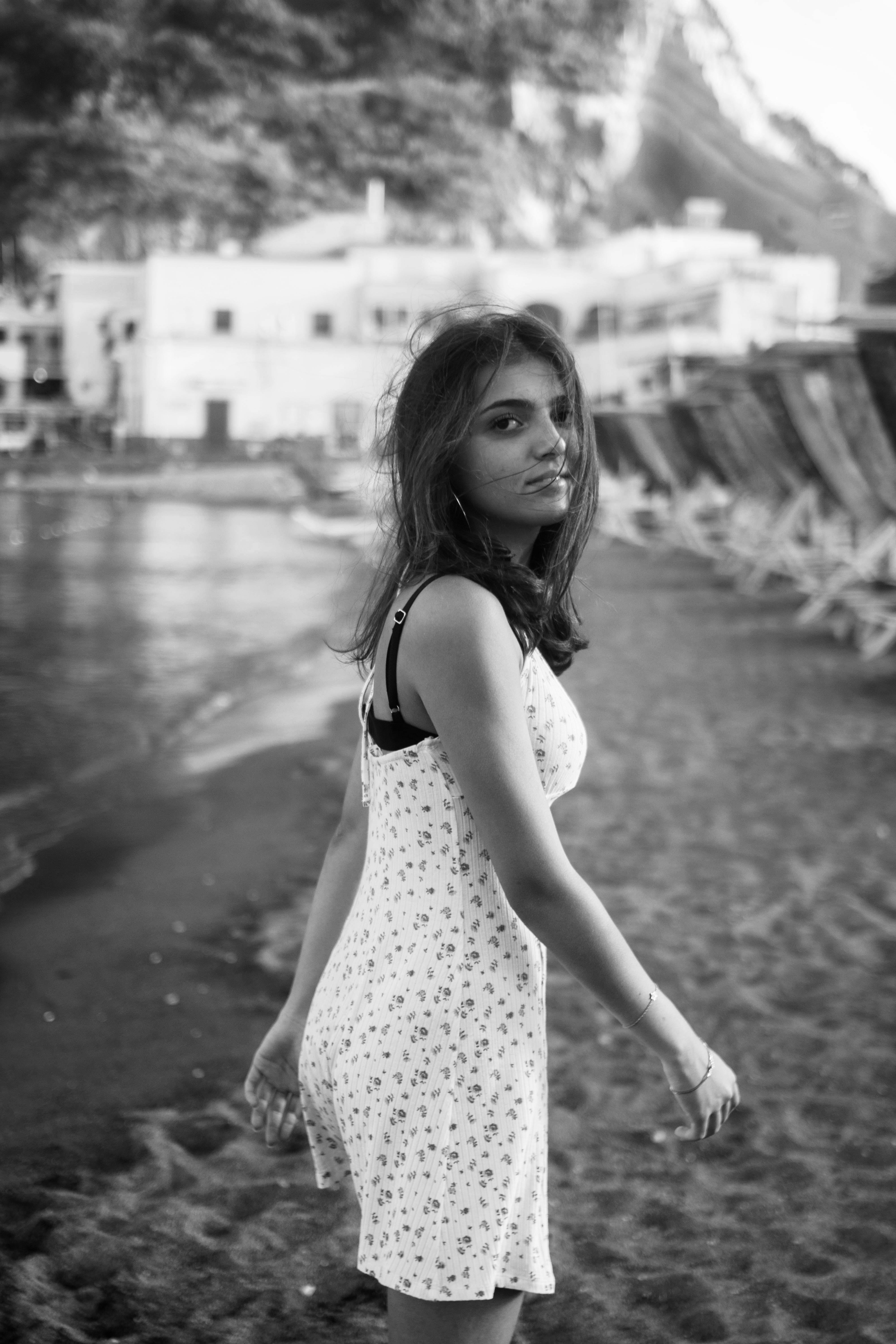 Black and white photo of a young woman walking on a beach in a summer dress.