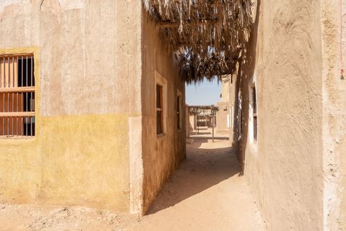 Free Authentic desert village alley with mud-brick houses and sandy path under a sunny sky. Stock Photo