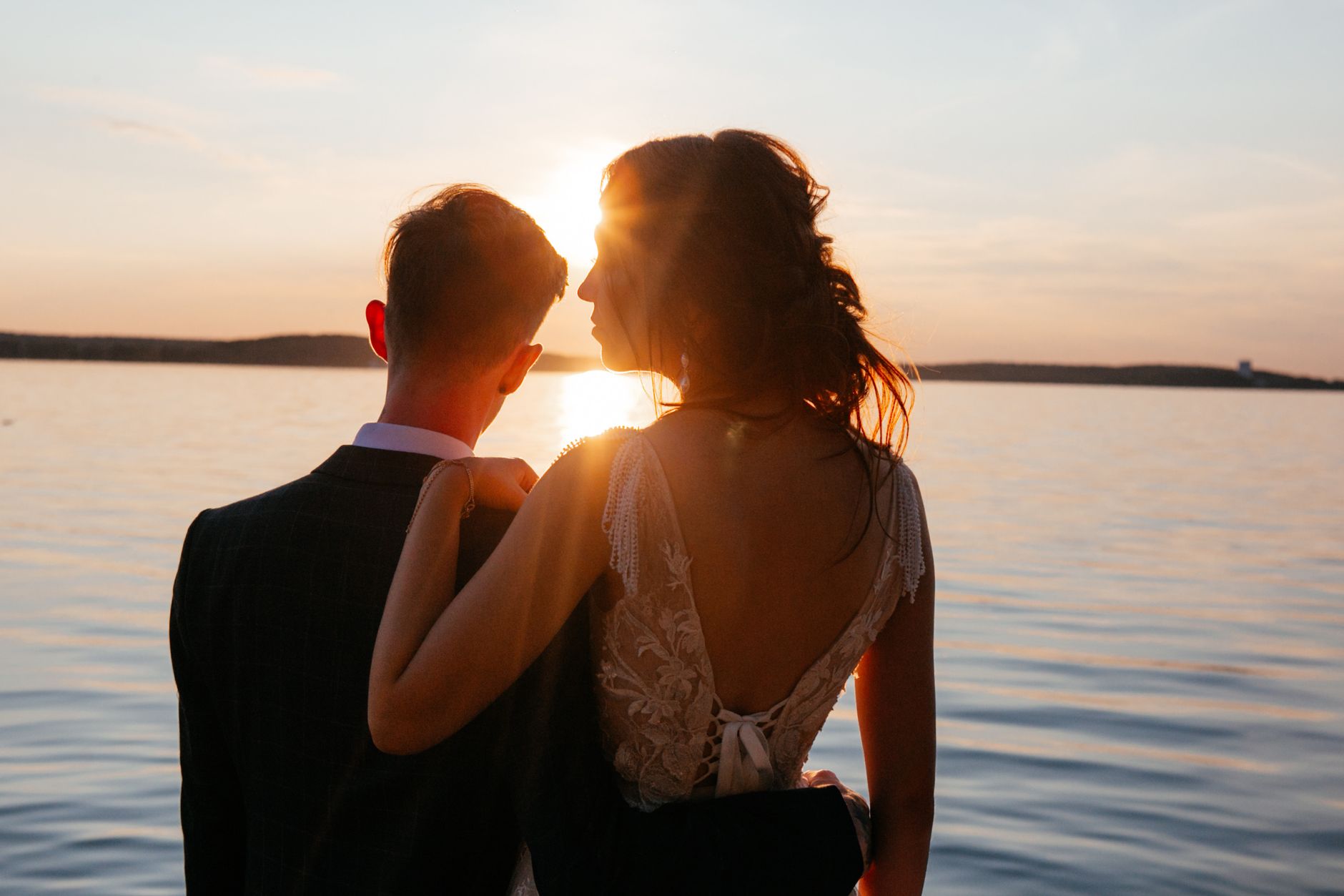 A couple embracing by a serene lake at sunset, capturing a romantic wedding moment.