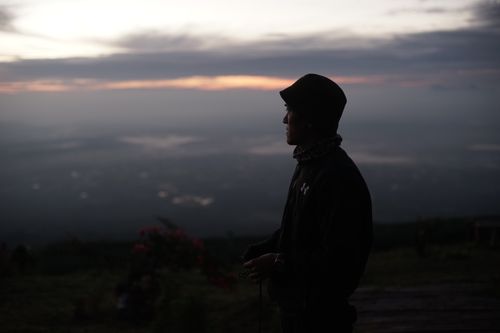 Free Silhouette of a man in a bucket hat standing on a hillside at sunset. Stock Photo