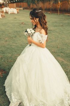 Beautiful bride in a wedding dress holding a bouquet in an outdoor garden setting at sunset.