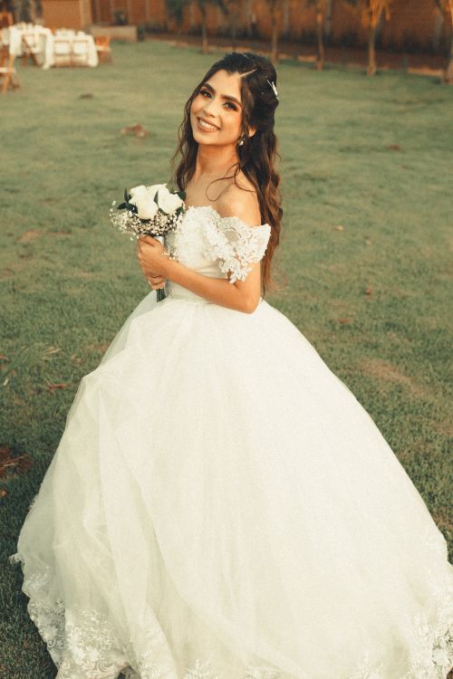Free A joyful bride in a white wedding dress holds a bouquet while smiling in an outdoor setting. Stock Photo