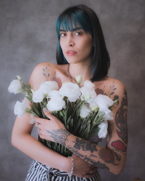 Photo of a Woman in Blue Hair and Tattoos Holding White Roses