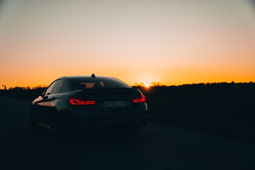 Free Silhouette of a car with illuminated taillights on a rural road during sunset. Stock Photo