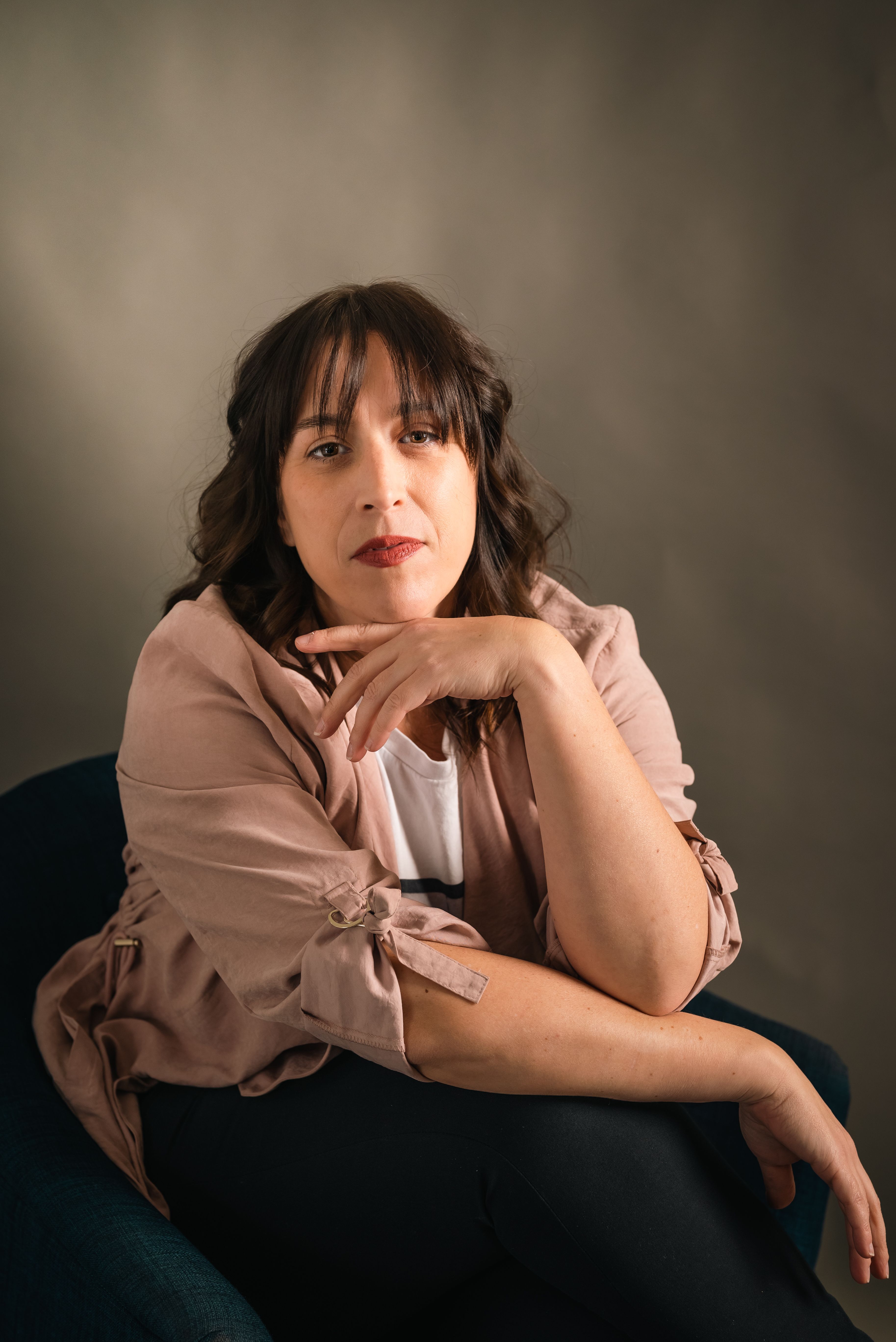 A woman with brunette hair, seated elegantly, exudes confidence in a thoughtful pose.