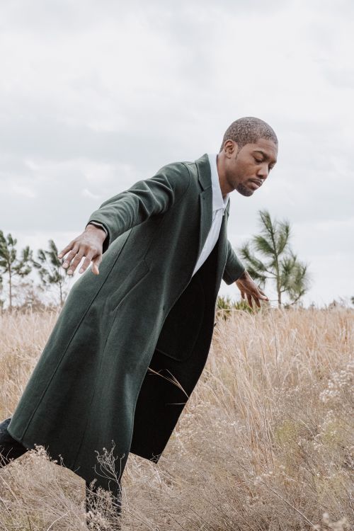 Free A man in a long coat poses outdoors, blending fashion with the tranquility of nature. Stock Photo