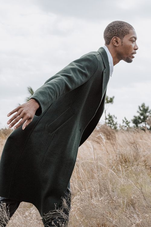 Free Portrait of a man in a green coat posing in a rural landscape, showcasing modern fashion style. Stock Photo
