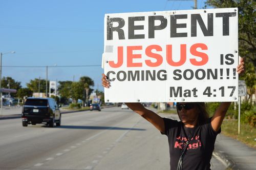 Free Woman holding a religious billboard on a street, emphasizing faith and repentance. Stock Photo