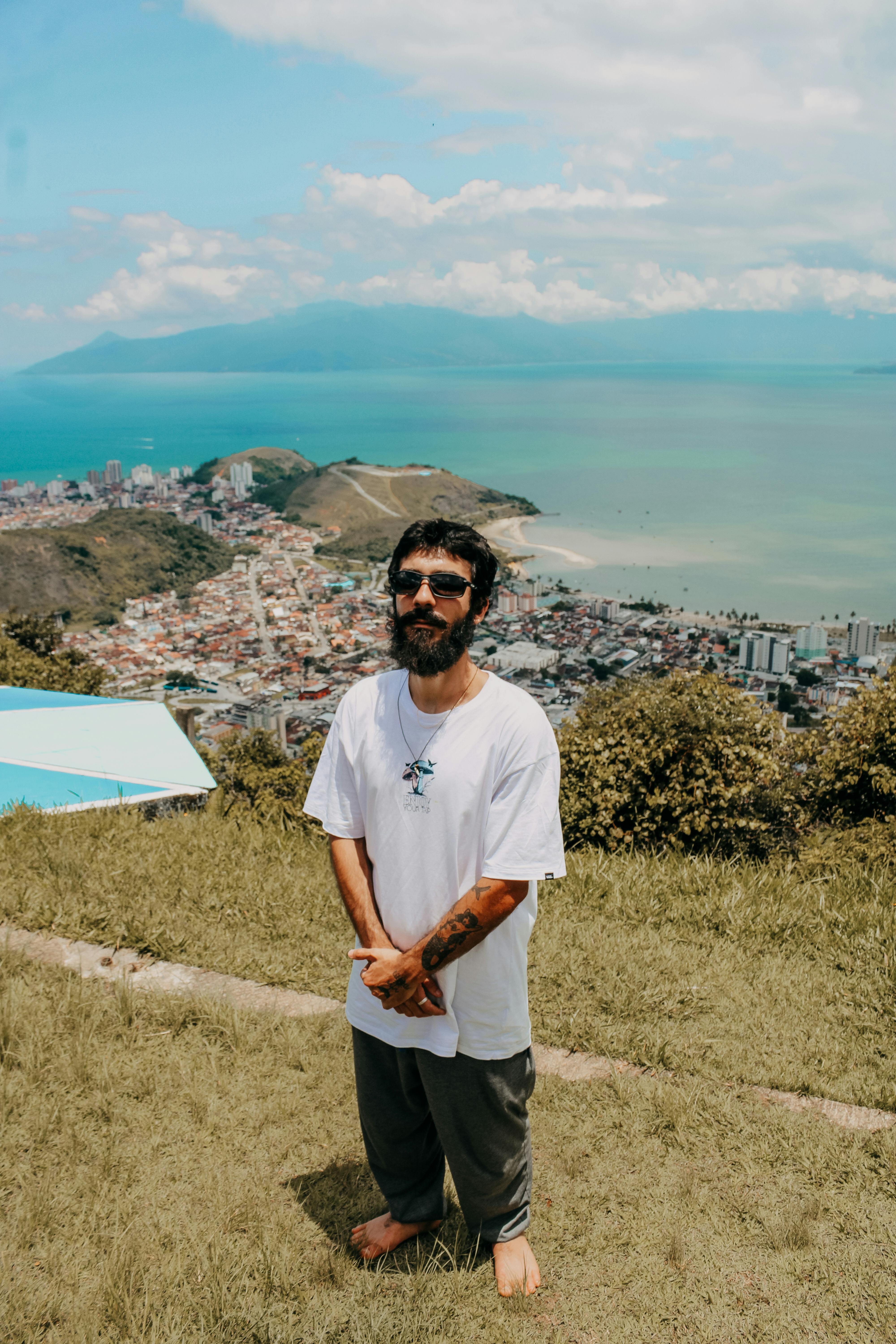 A young man with sunglasses enjoys a sunny day overlooking Paraty's coastal landscape.