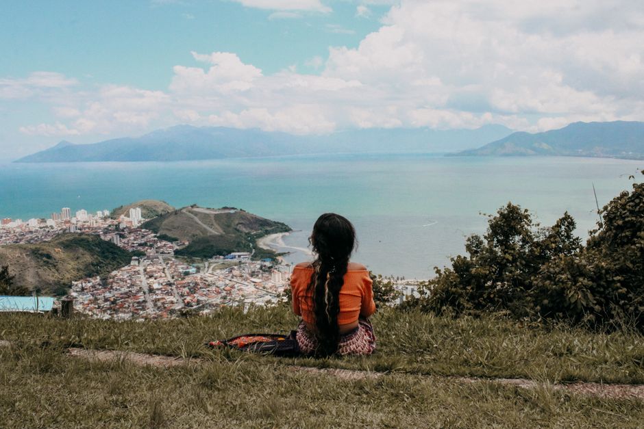 7 Dicas para Viajar Sozinha e se Sentir Empoderada 2 A woman with long hair enjoys the scenic ocean and city view from a hilltop in Paraty, Brazil.