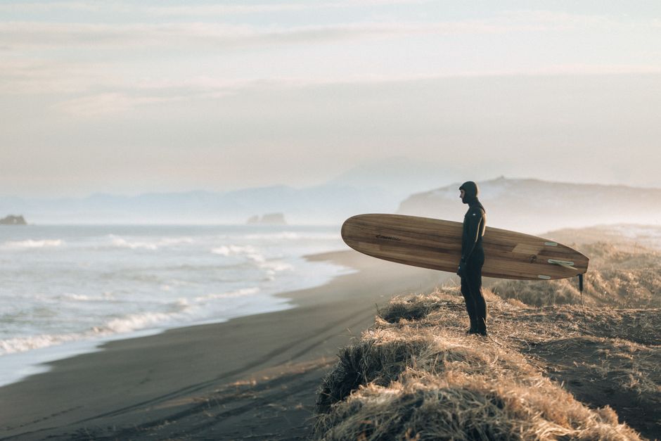 Surfer on foggy Kamchatka coast holding board, ready for ocean waves.