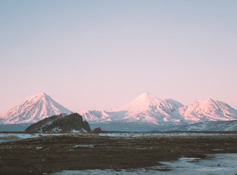 Experience the serene beauty of snow-capped mountains in Kamchatka at sunrise, captured in a tranquil winter setting.
