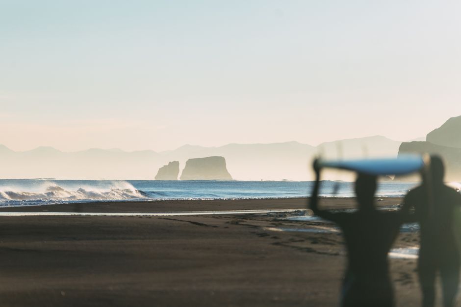 Silhouettes of surfers with boards on a beautiful Kamchatka beach at sunrise.