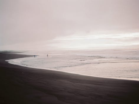 A tranquil beach scene in Kamchatka Krai, Russia, with soft waves and distant figures.