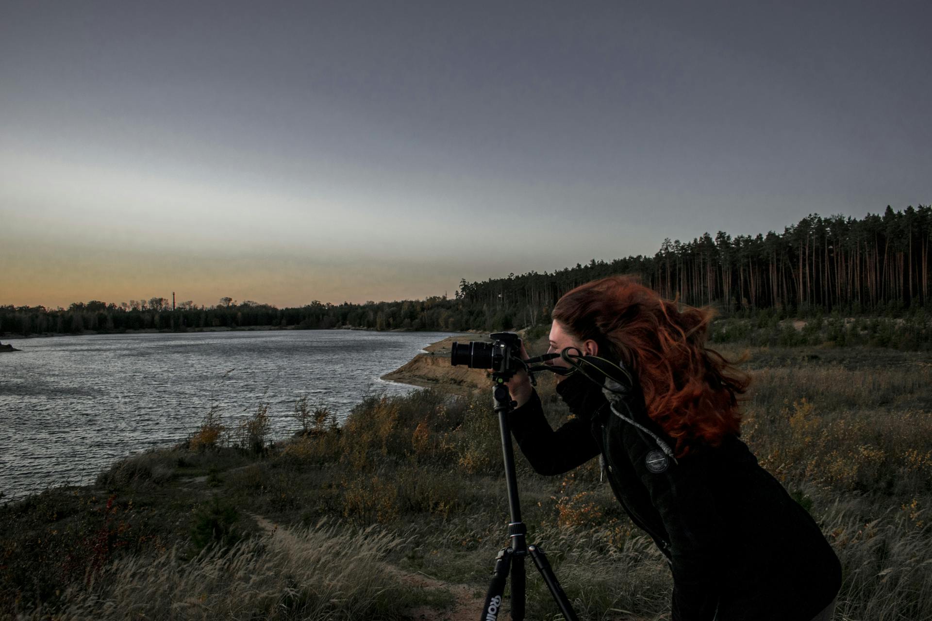 A woman photographer captures a serene sunset by a lakeside in Golčův Jeníkov, Czechia.