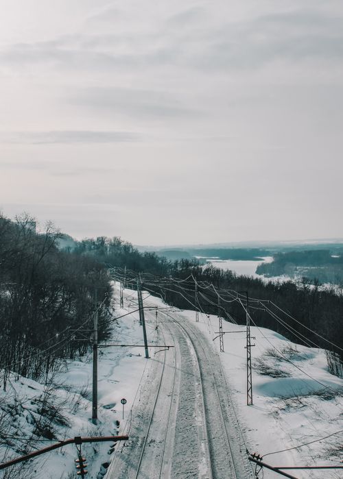 Free Aerial view of a snow-covered railway in a serene winter landscape with bare trees and an overcast sky. Stock Photo