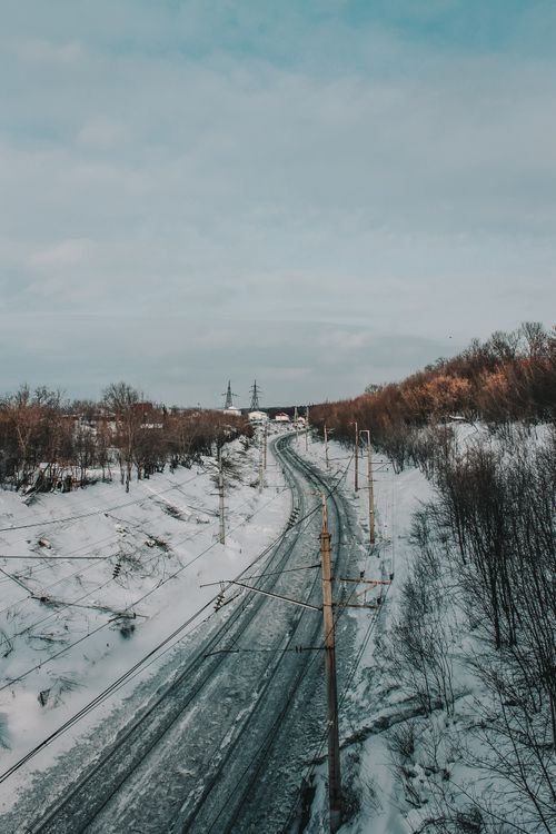 Free A serene winter landscape featuring a snowy railway stretching through a calm countryside. Stock Photo