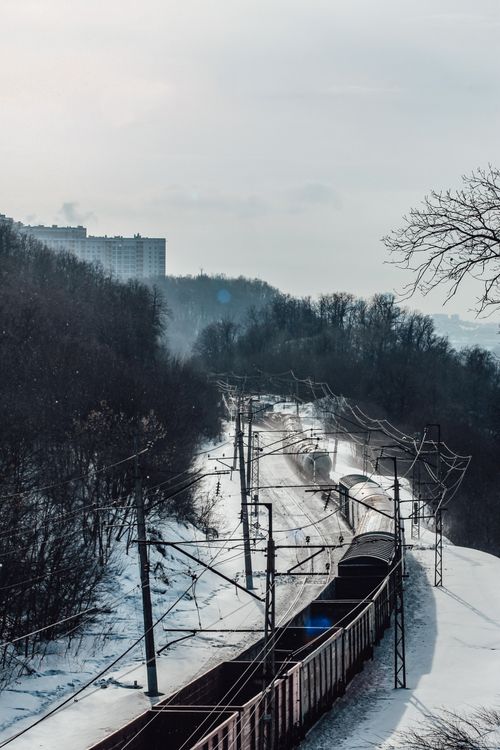Free A scenic train travels through a snowy winter landscape, flanked by trees and urban backdrop. Stock Photo