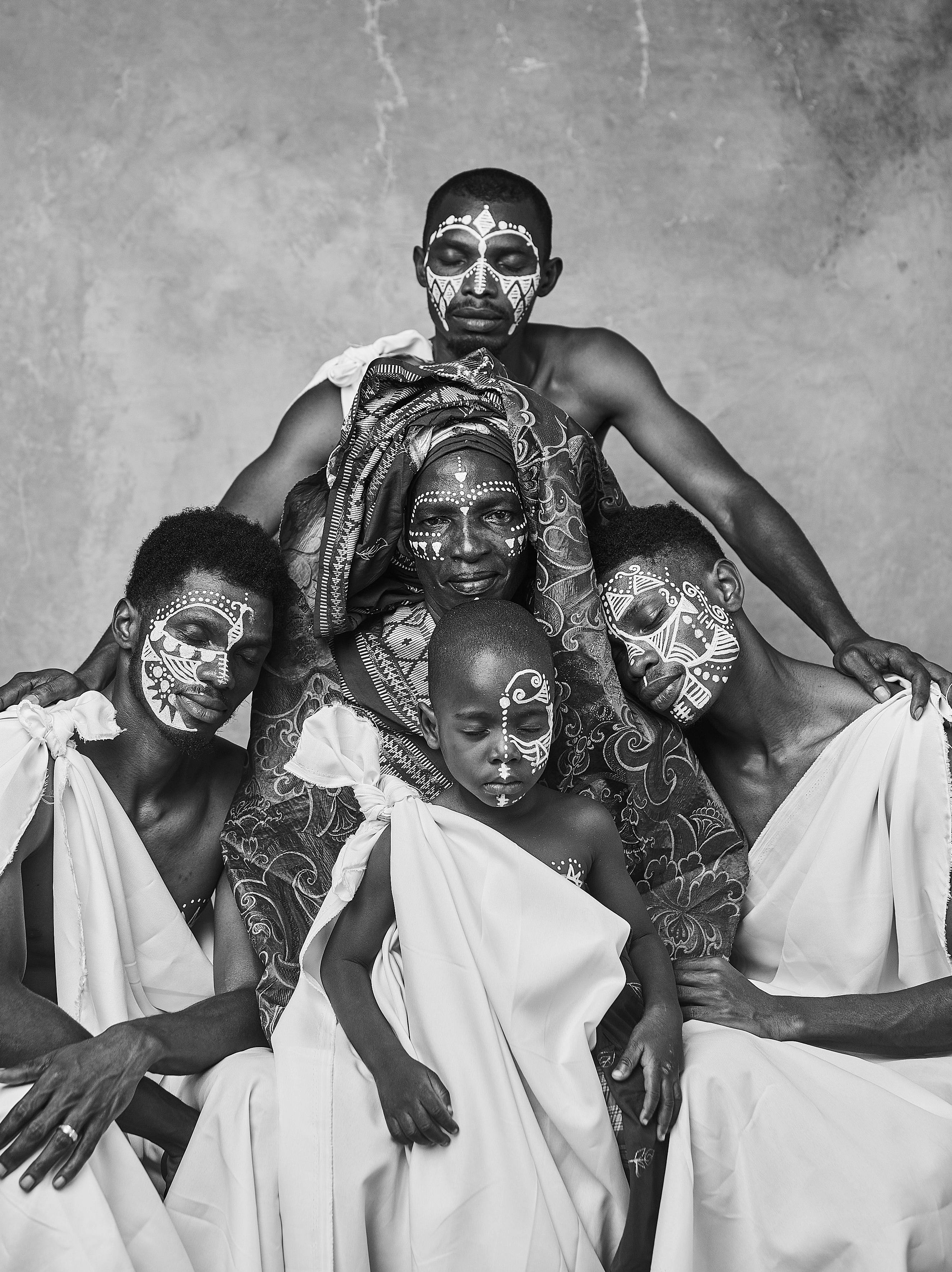 Black and white portrait of a Nigerian family with traditional face paint and white robes.