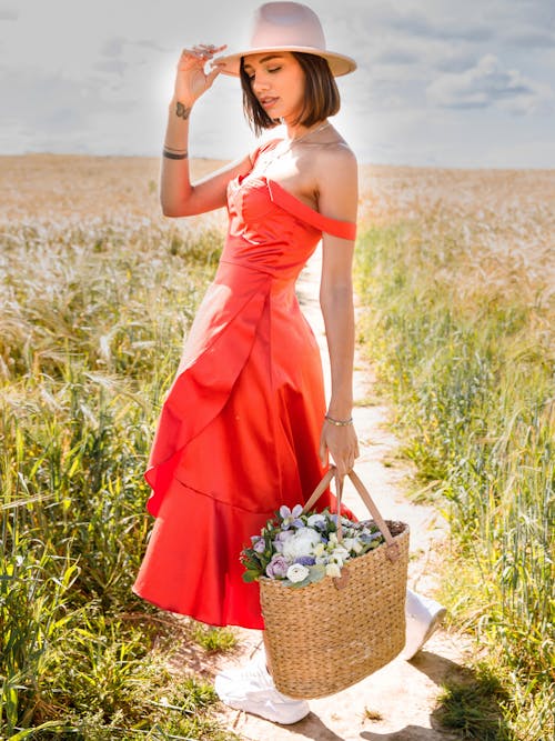 Woman in a Dress and a Hat Carrying a Basket of Flowers