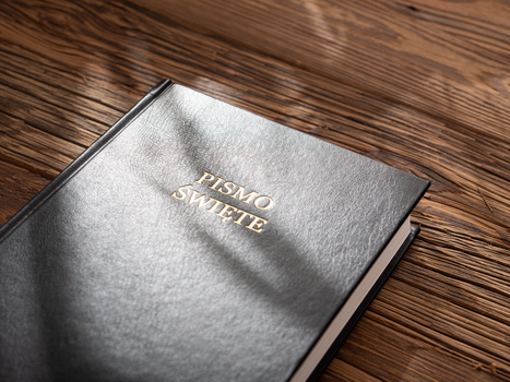 Close-up of a Polish Holy Bible with a black cover on a wooden table, sunlight casting shadows.