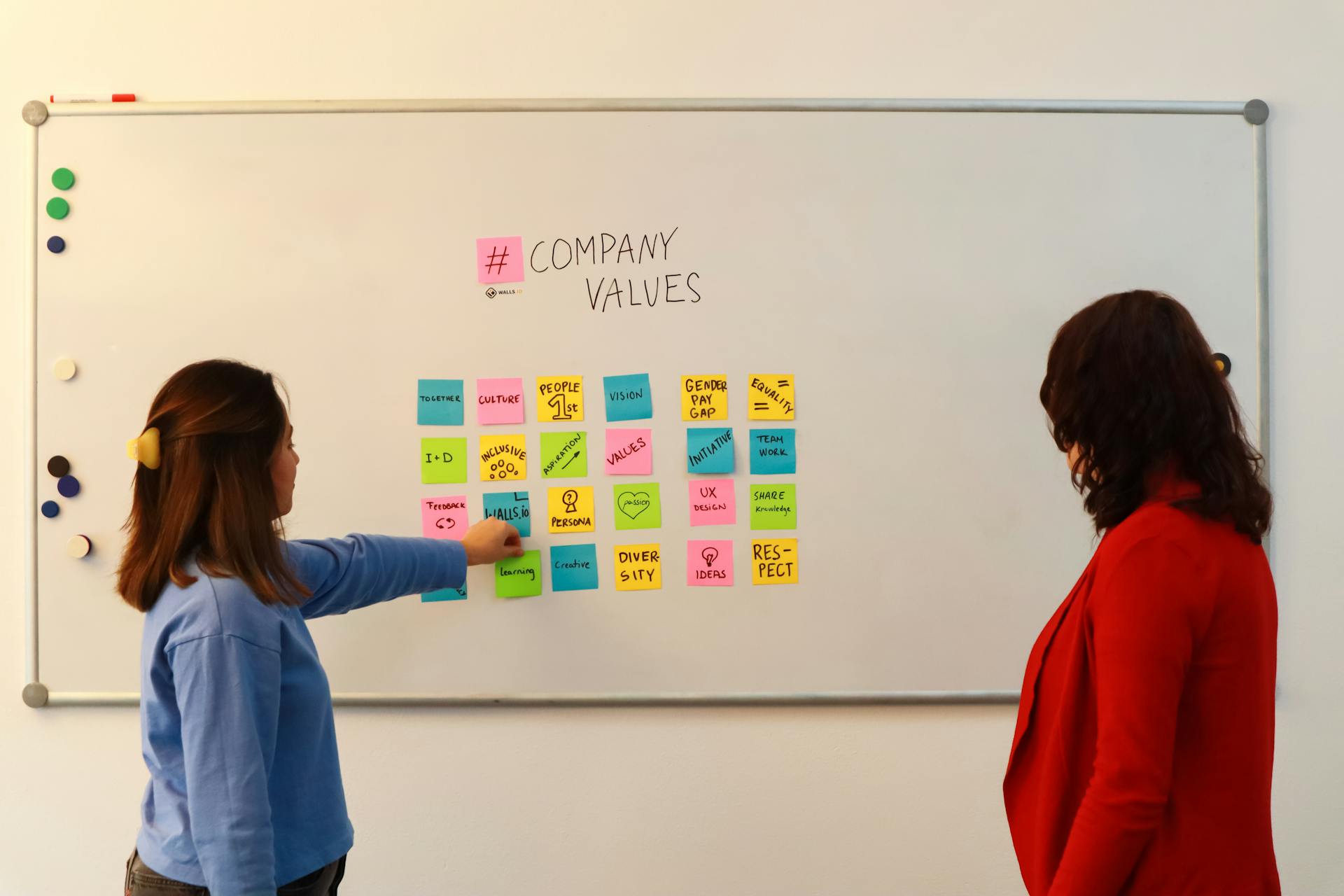 Two women in an office discussing company values on a whiteboard.