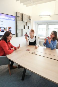 Three women playing cards in a modern office, creating a relaxed and sociable atmosphere during work hours.