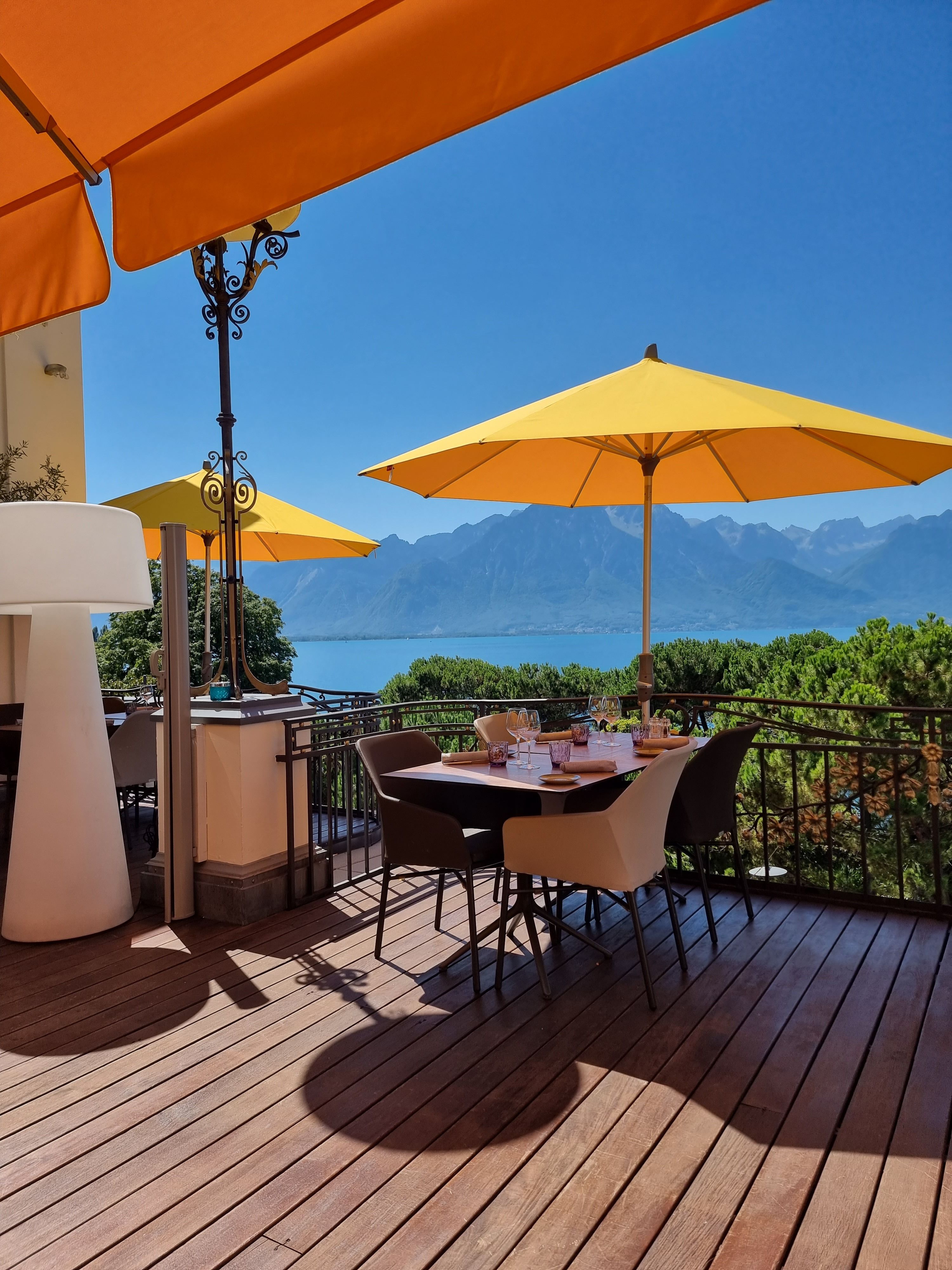 Terrasse dressée sous des parasols jaunes, face au lac et aux montagnes
