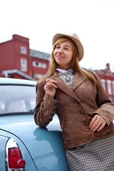 A young woman in retro fashion leans on a vintage car, smiling confidently.
