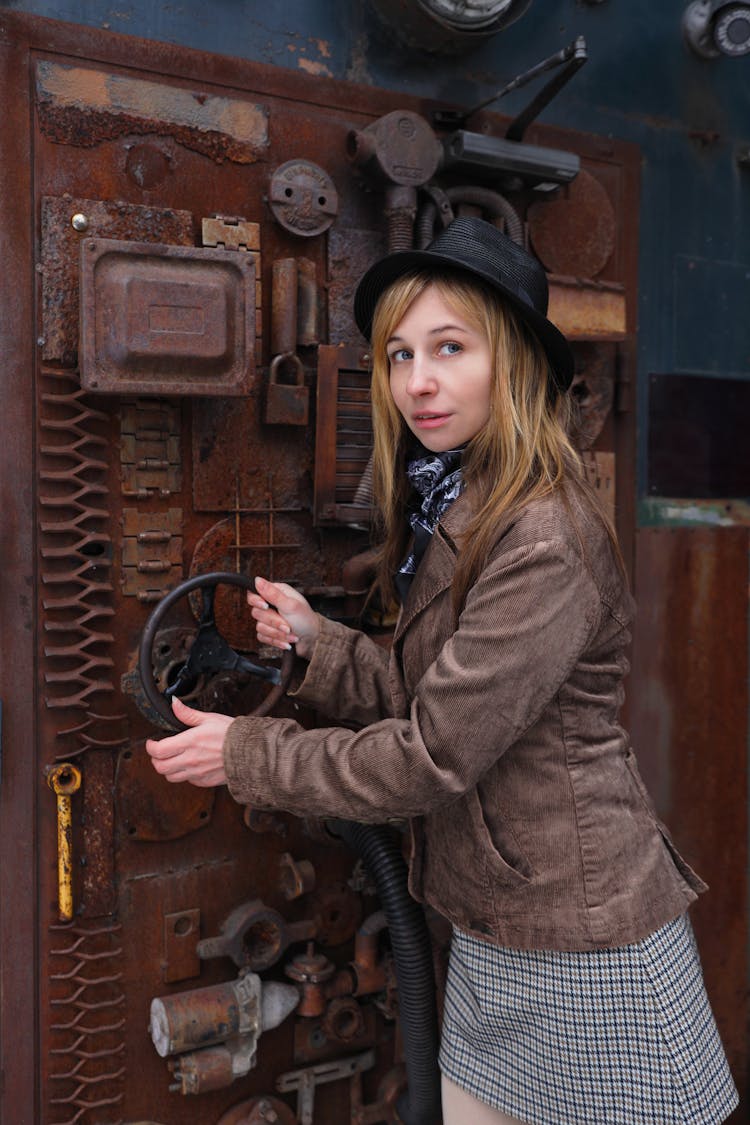 Woman In A Hat Holding A Wheel Of A Rusty Piece Of Equipment