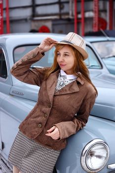 Stylish young woman leaning on a classic car, exuding vintage charm.