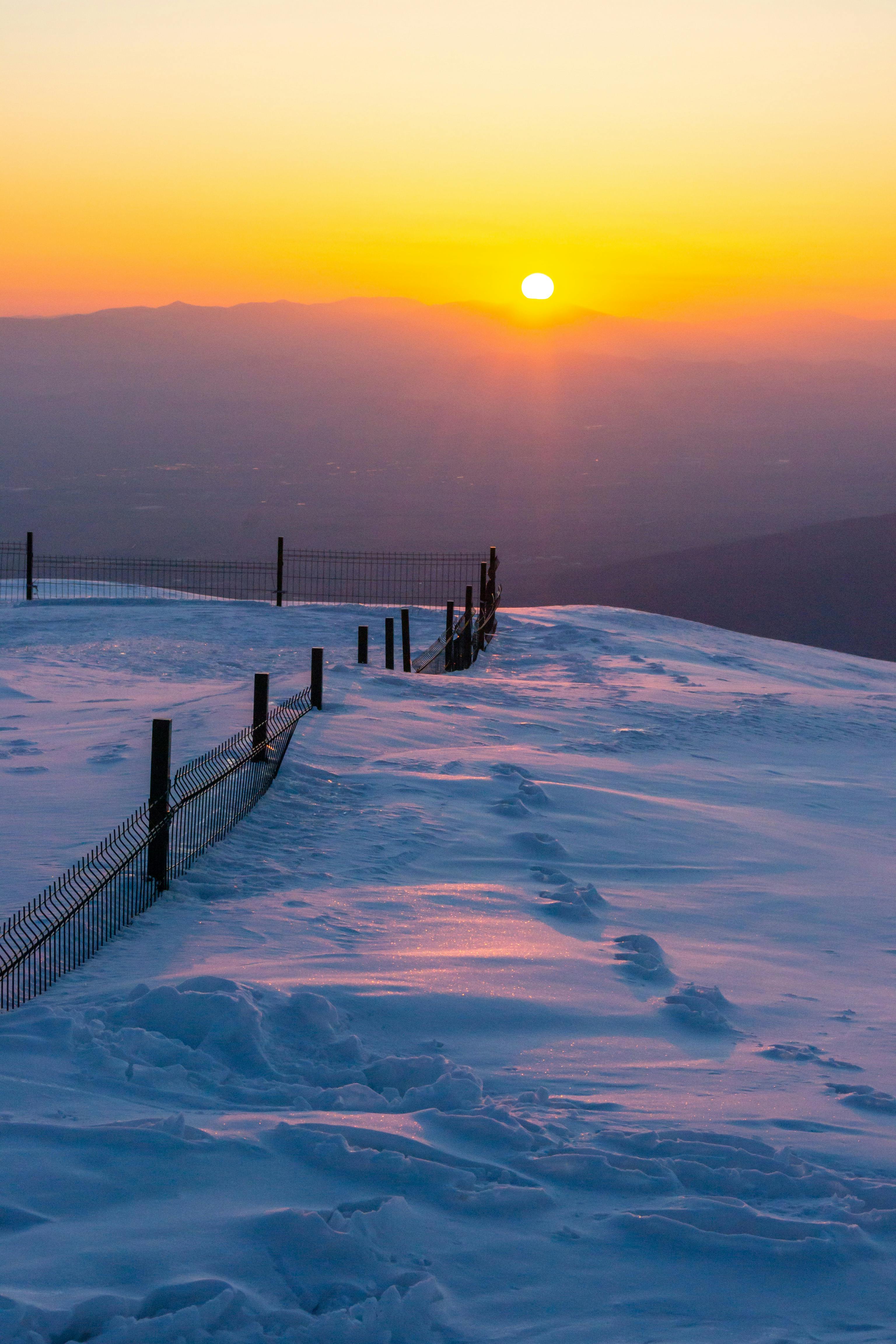 Serene winter sunset over snowy landscape at Cherni Vrah, Bulgaria with a tranquil orange sky.