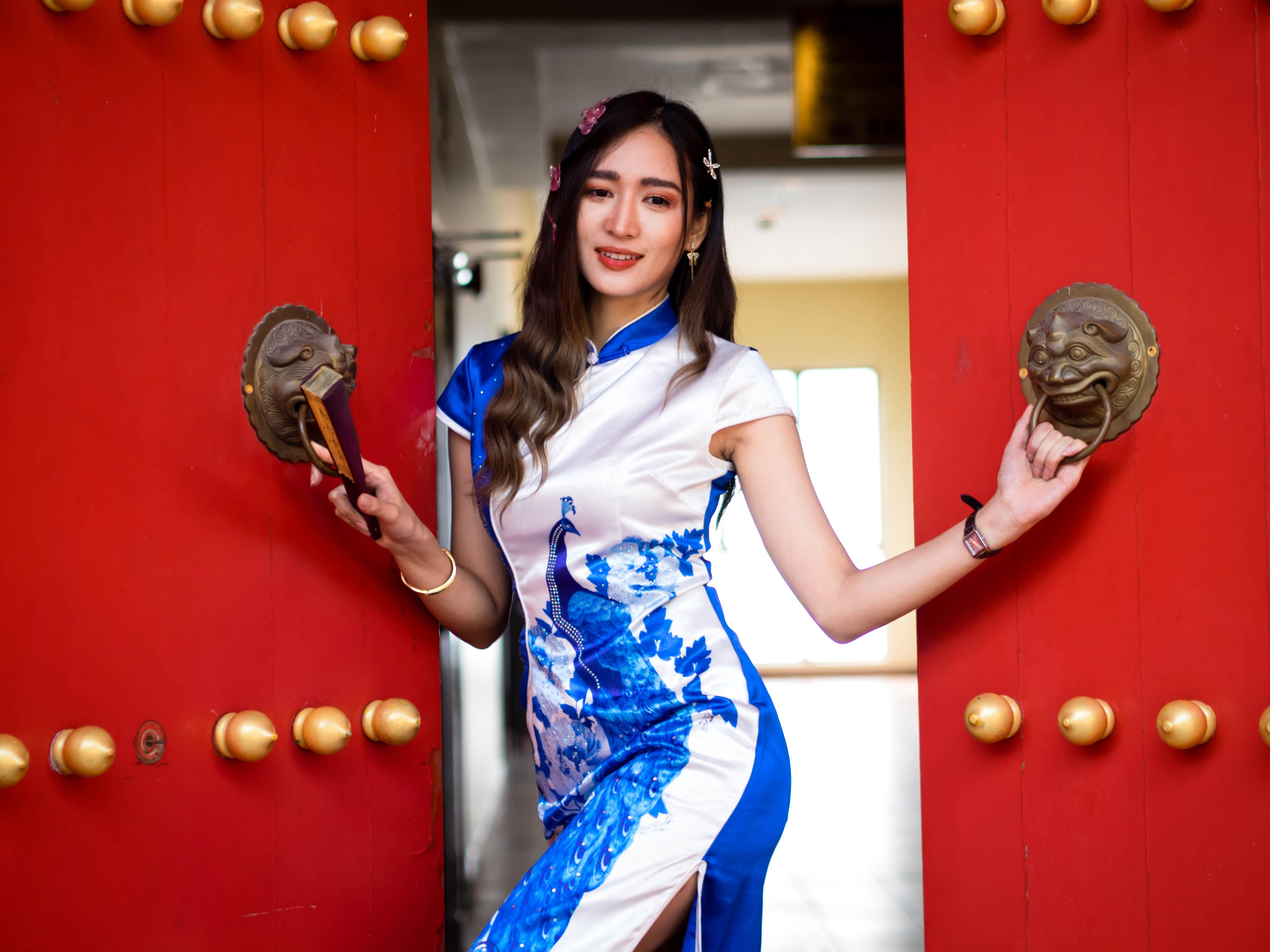 Portrait of a smiling woman in traditional clothing posing by an ornate red door.