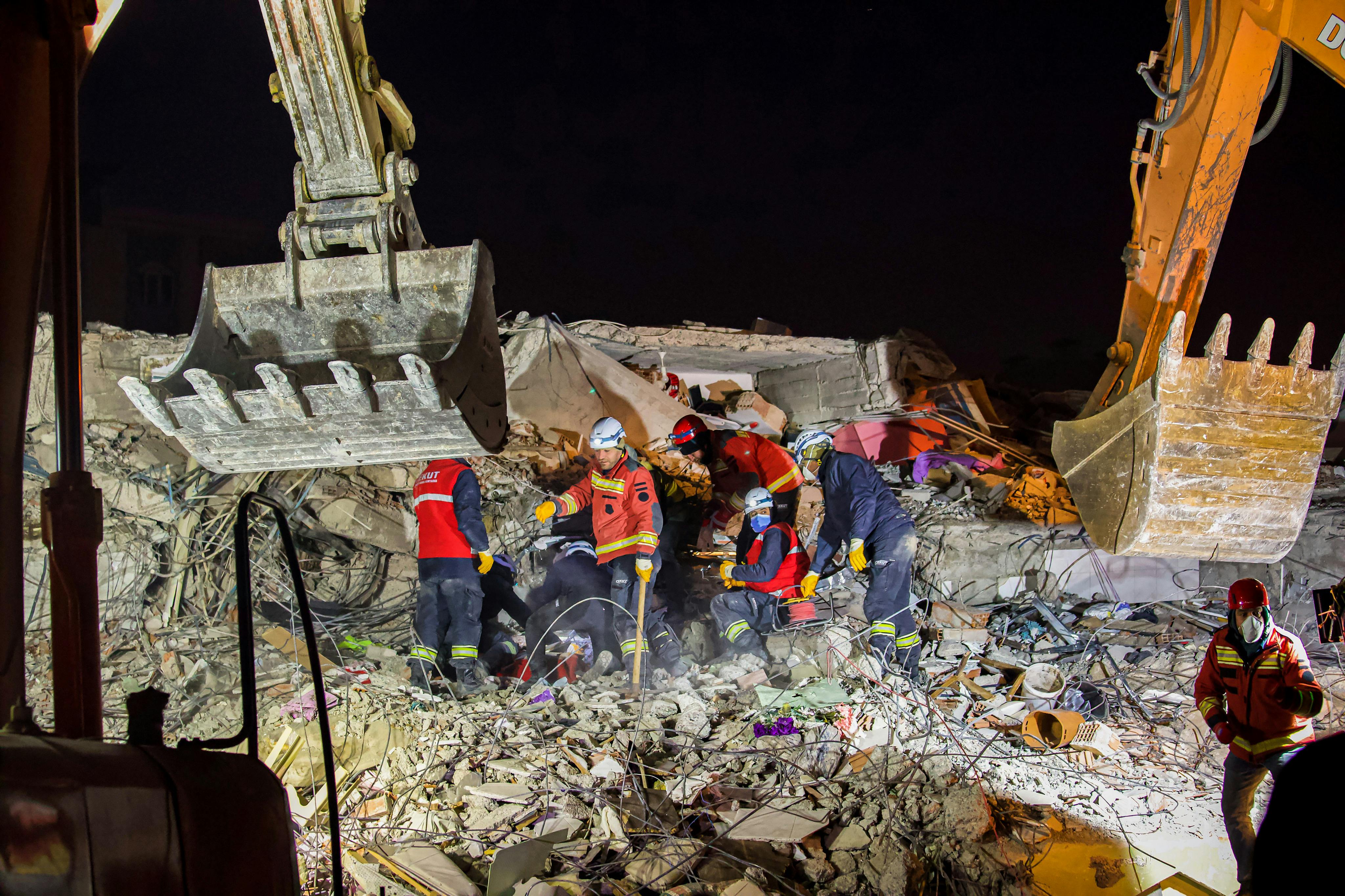 Emergency workers conduct a nighttime rescue amidst earthquake debris and heavy machinery.