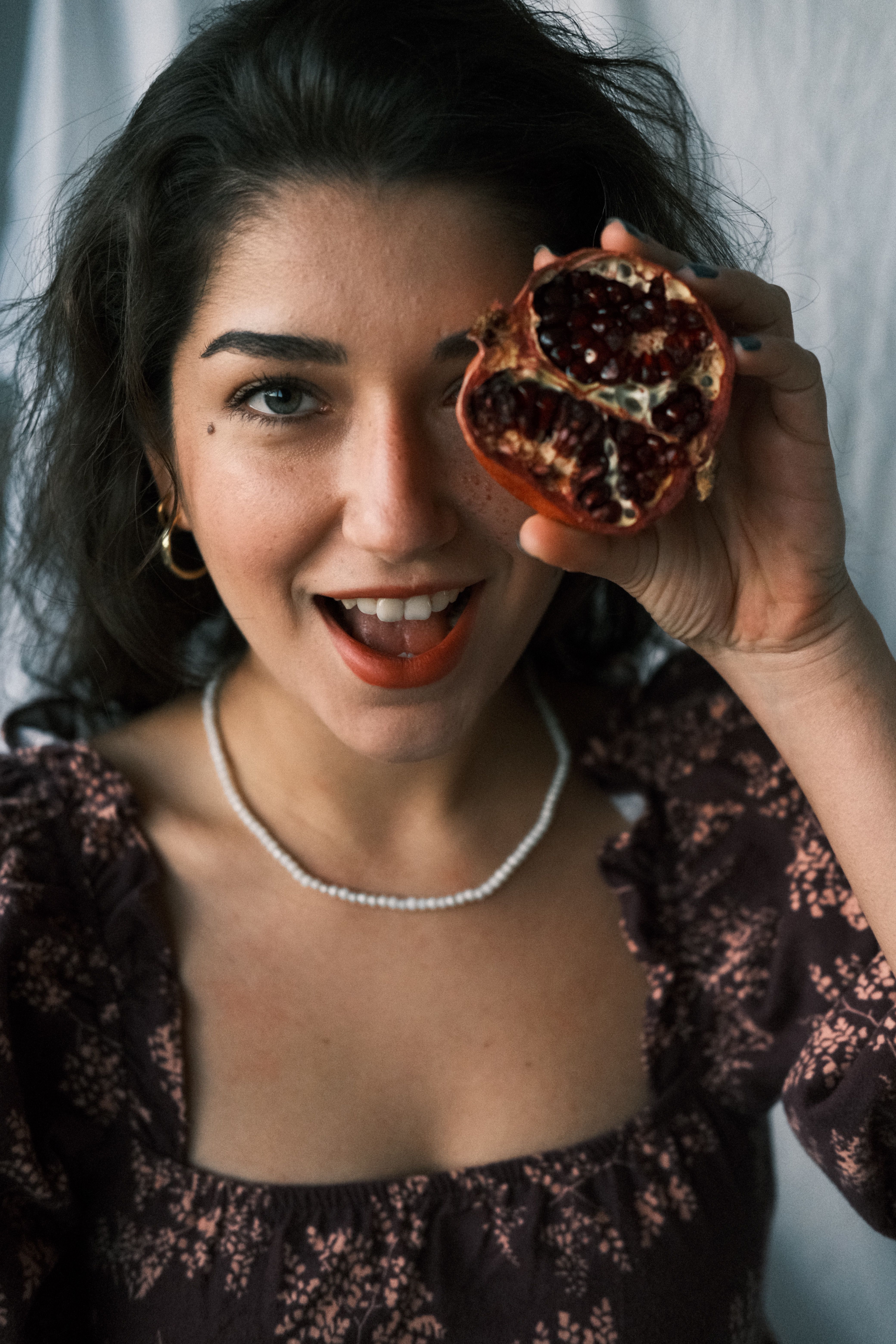 Cheerful woman with pomegranate slice in playful portrait. Capturing natural beauty and freshness.